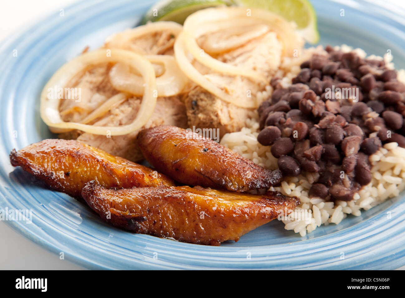 Nahaufnahme des kubanischen Abendessen mit Fokus auf frittierte süße Kochbananen. Marinierter Schweinebraten mit schwarzen Bohnen und Reis runden die Mahlzeit ab. Stockfoto
