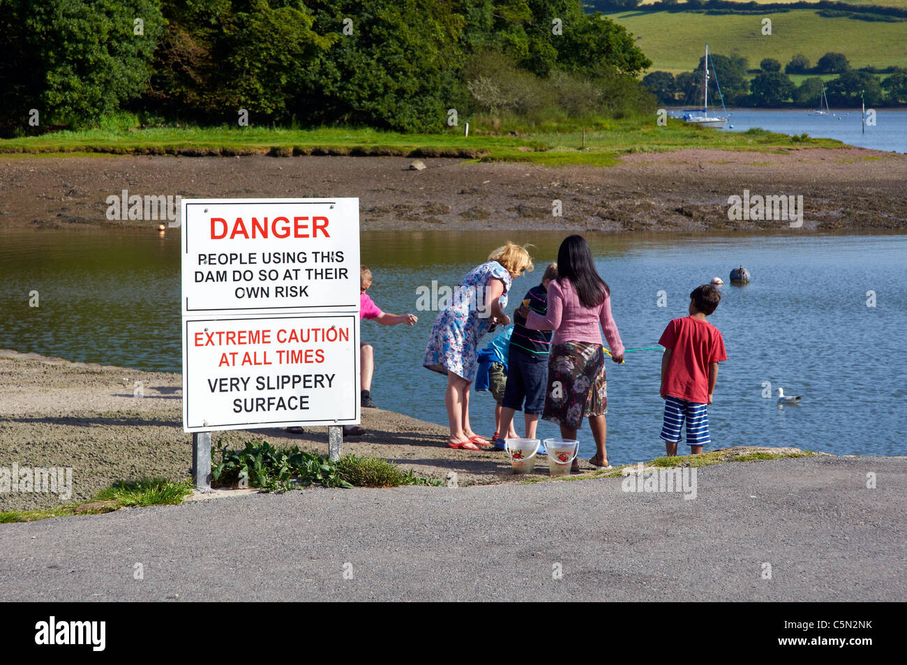 Kinder von der Staumauer für ein Gezeiten-Mühlenteich bei Stoke Gabriel auf dem River Dart ignorieren Sicherheitshinweise Verdrehungen Stockfoto