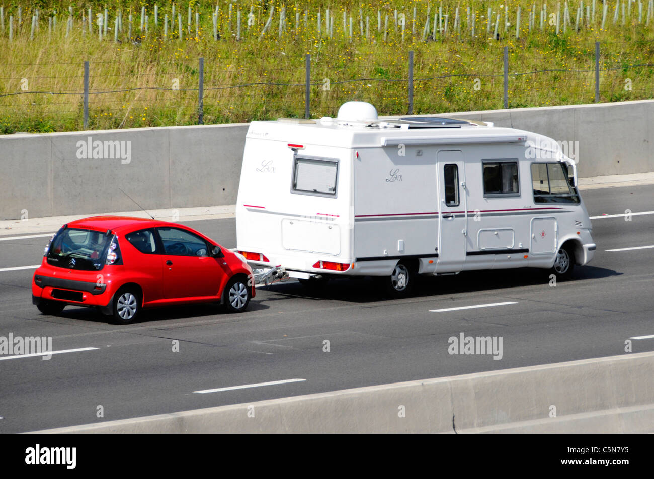 Seiten- und Rückansicht des Französischen weißen Le Voyageur LVX Wohnmobil abschleppen rot Citreon C1 Auto Auf de Autobahn fahren für eine Reisen Lifestyle Stockfoto
