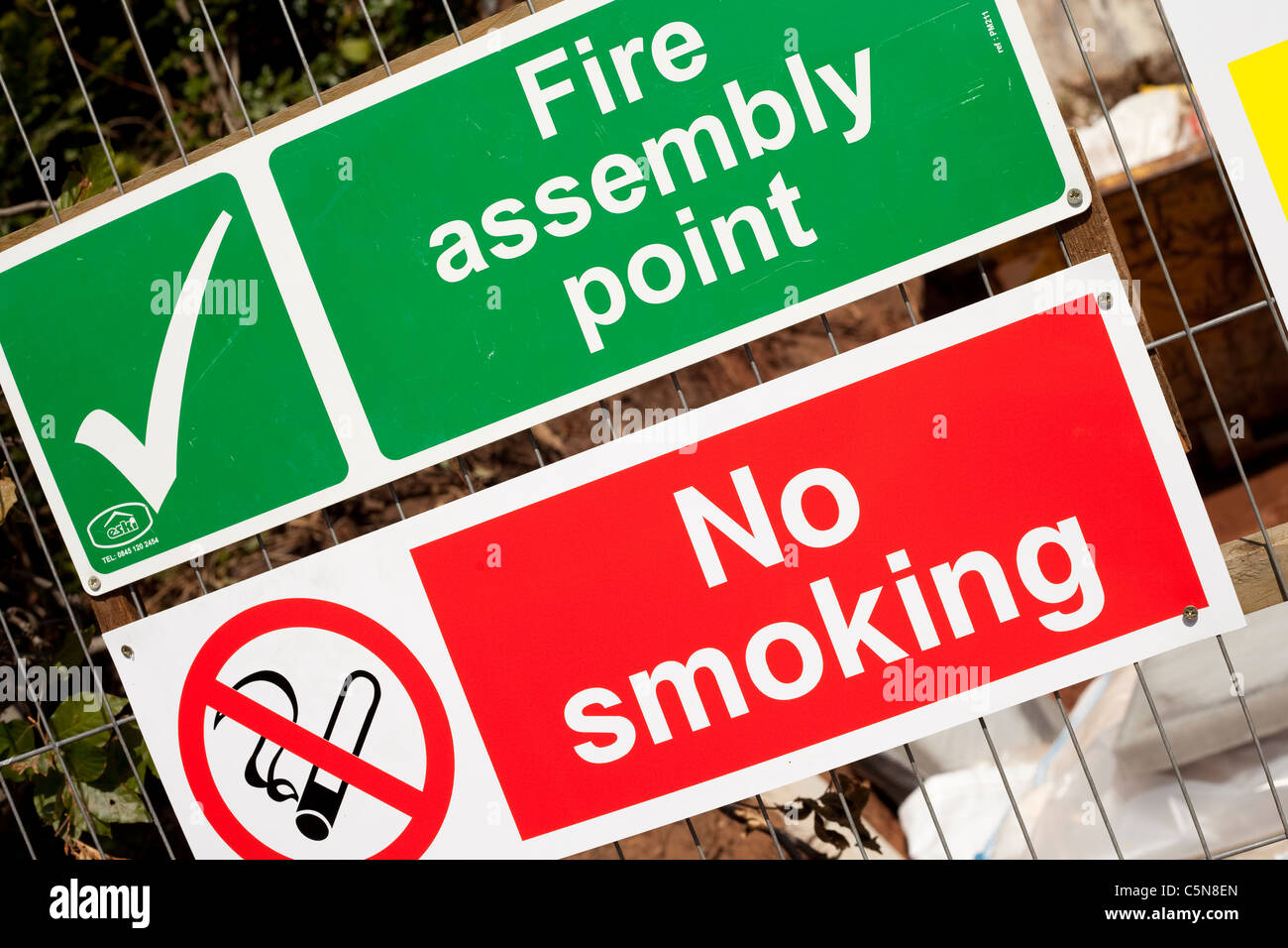 Ein grünes und weißes Feuer Sammelplatz zu signieren, roten und weißen No Smoking Schild auf einer Baustelle England UK Stockfoto