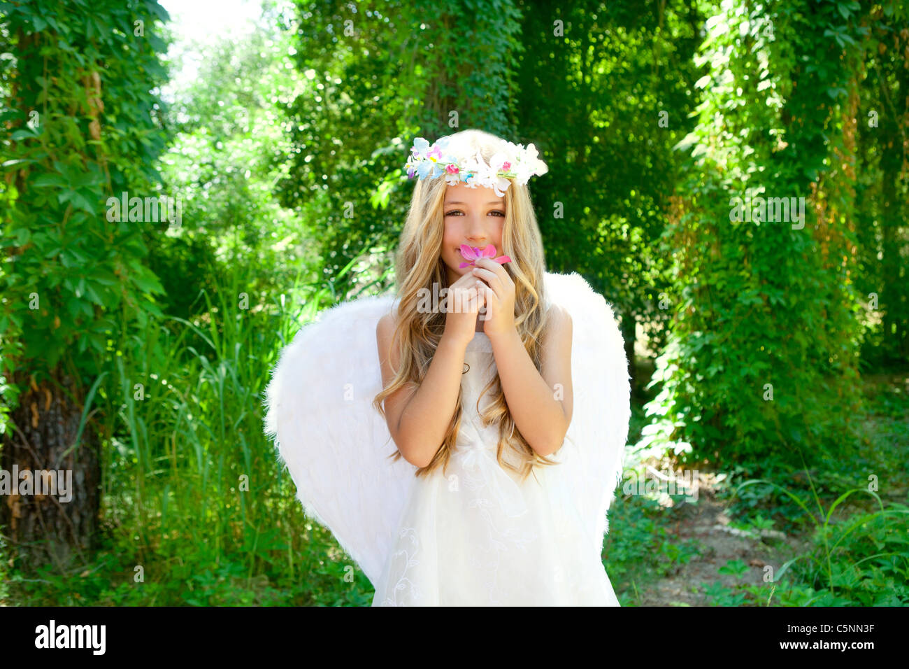 Engel Kinder Mädchen riechen rosa Blume im Wald mit weißen Flügeln und Krone Stockfoto