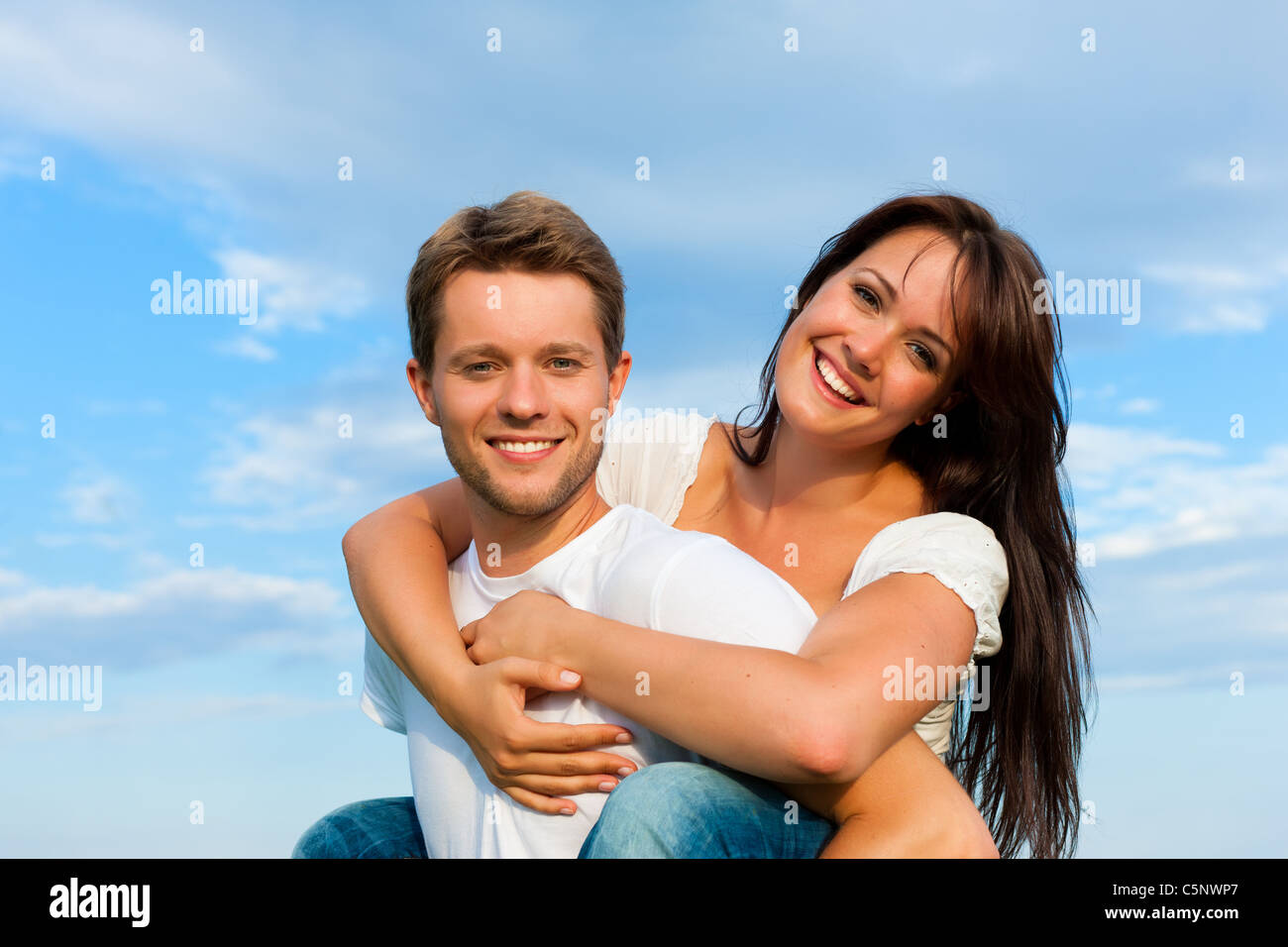 Glückliches Paar unter blauem Himmel; Er ist ihr Huckepack tragen. Stockfoto