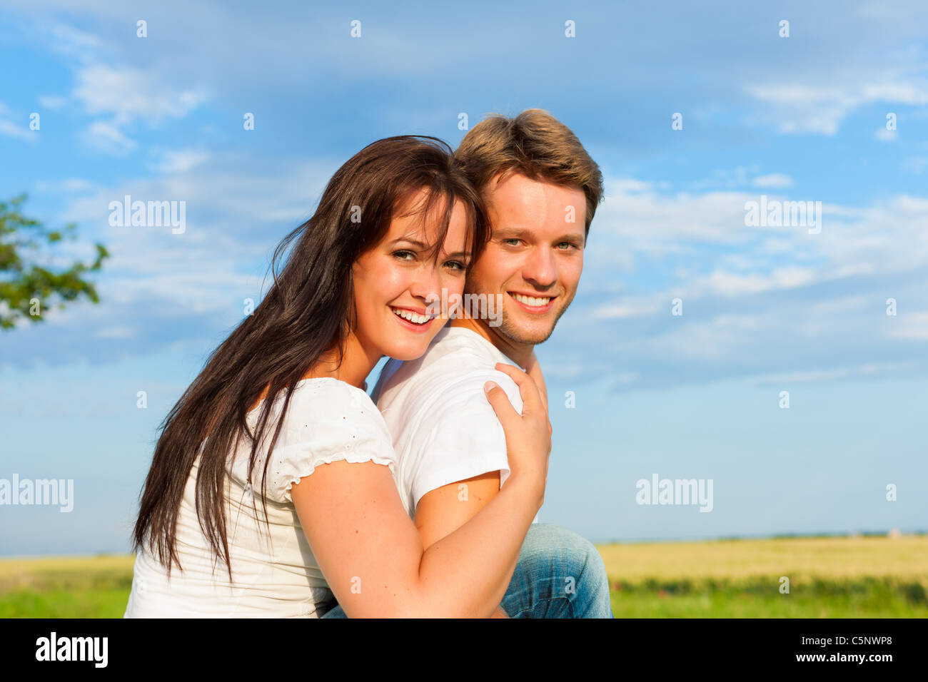 Glückliche Paar auf einer Wiese im Sommer, ist Mann seine Frau Huckepack tragen Stockfoto