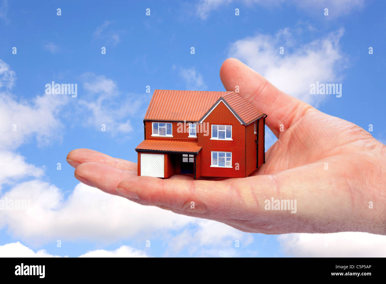 Foto von einer Hand hält ein Musterhaus Himmel im Hintergrund. Stockfoto