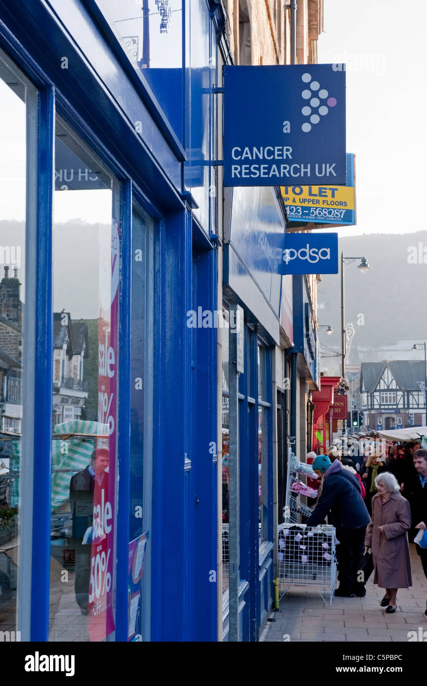 Geschäftige Hauptstraße am Wintermarkttag, Leute einkaufen an Ständen und Reihe von Charity-Shops (Cancer Research UK, PDSA) - Otley, West Yorkshire, England. Stockfoto