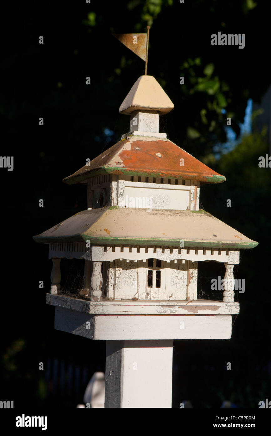 Weißer Vogelhaus mit Metalldach und Fahne an der Spitze in der Nähe von Bürgersteig. Stockfoto