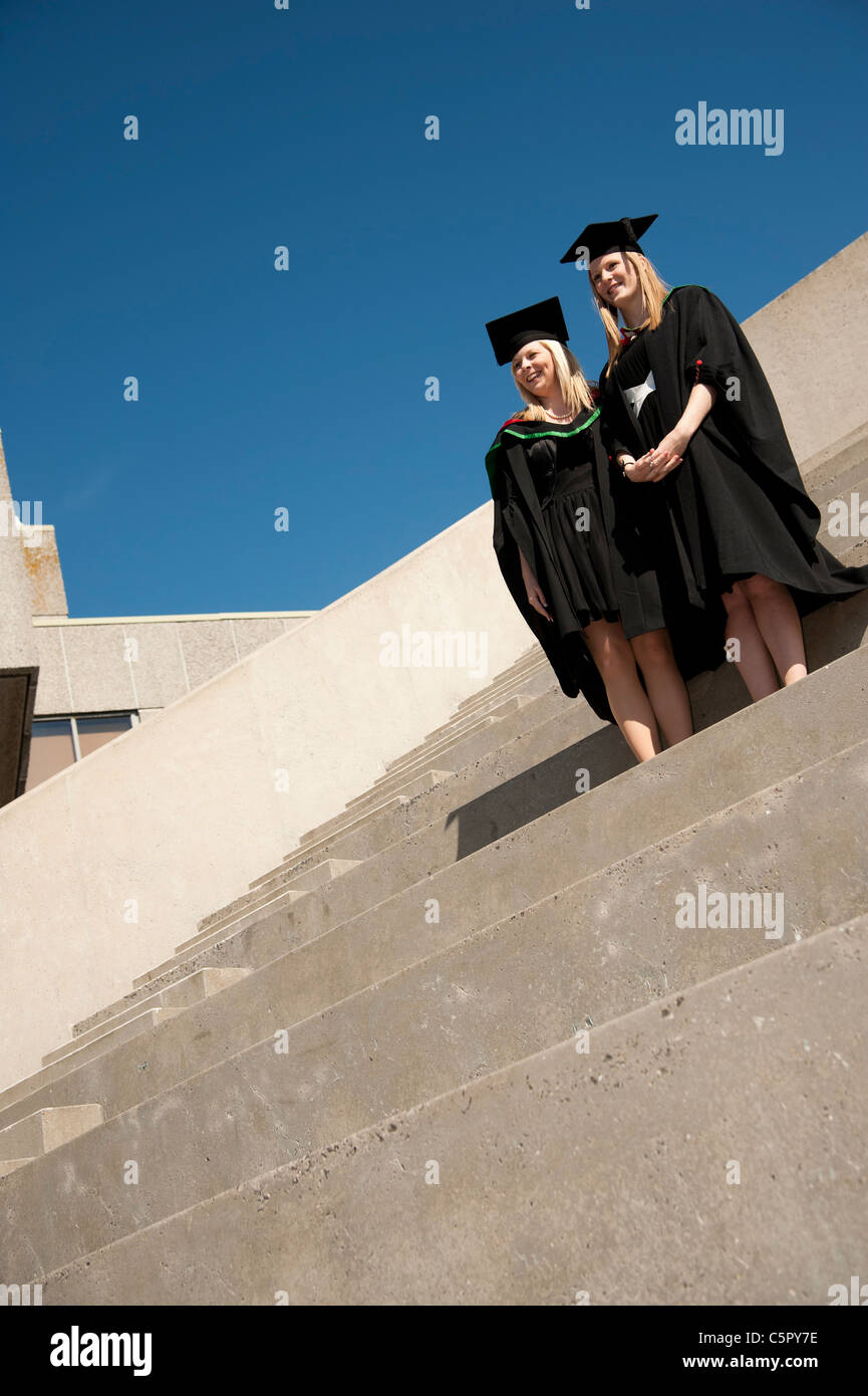 Zwei weibliche Aberystwyth Universität Absolventen auf Graduierung Tag, UK, stehend auf konkrete Schritte, blauer Himmel Stockfoto