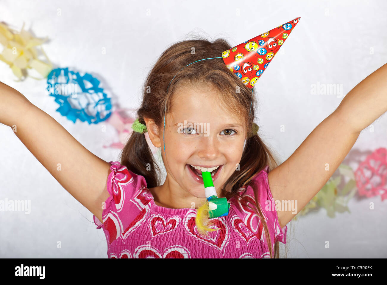 acht Jahre altes Mädchen mit Partyhut und Trompete auf einem Kinderfest Stockfoto