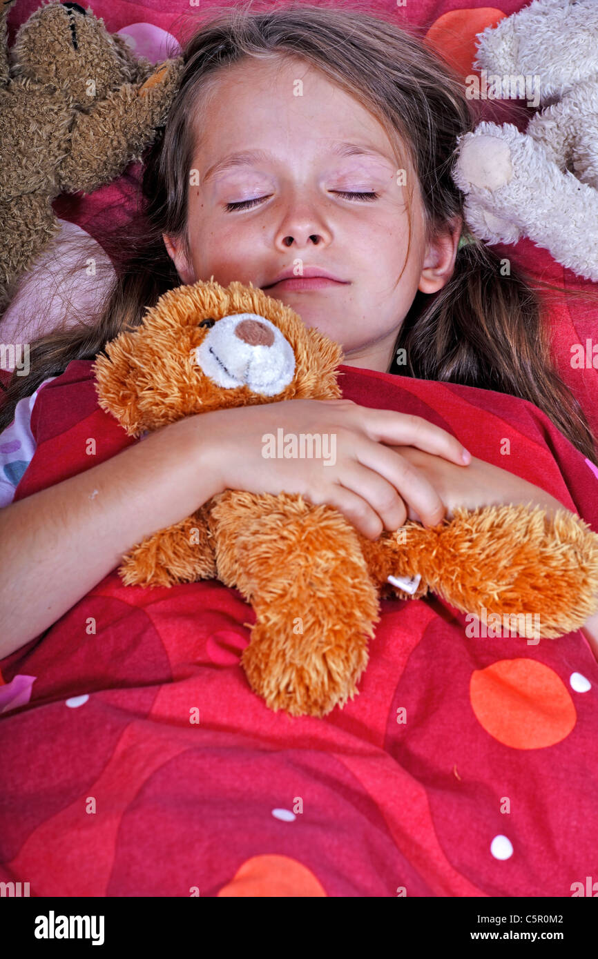 ein acht Jahre altes Mädchen im Bett mit Decke und Kissen und Stofftiere Stockfoto