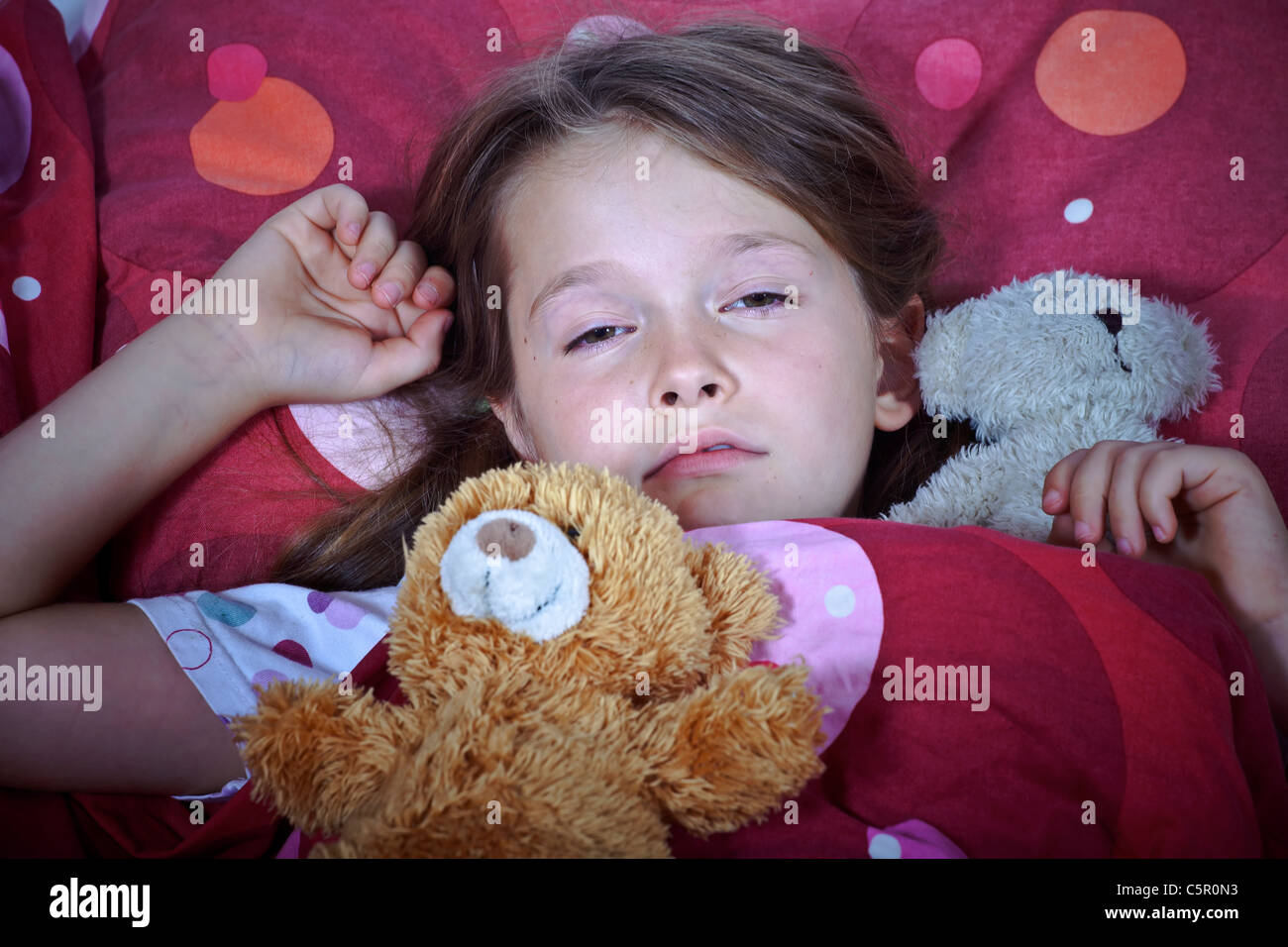 ein acht Jahre altes Mädchen im Bett mit Decke und Kissen und Stofftiere Stockfoto
