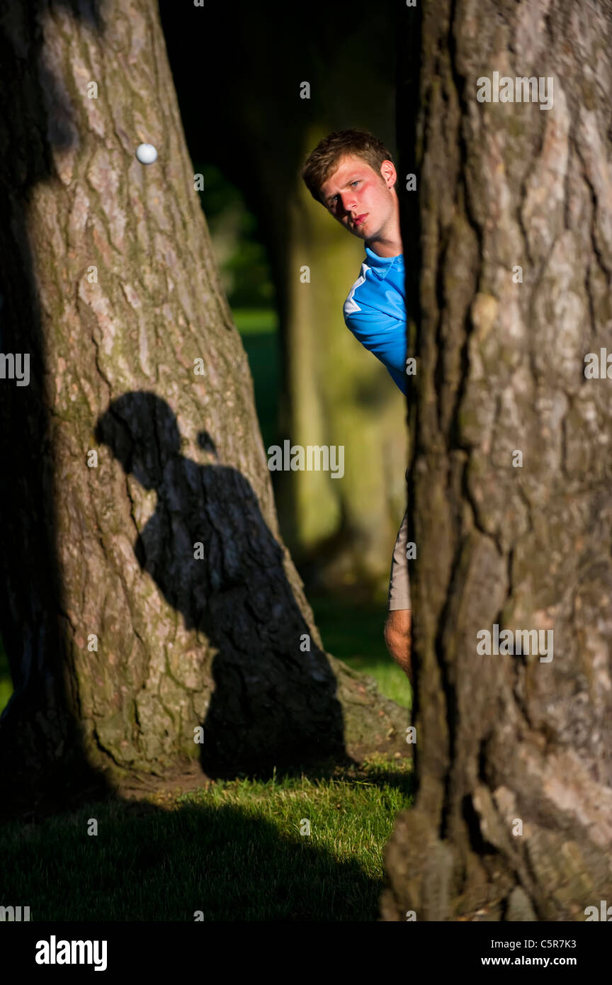 Ein Golfer spielt einen Schuss aus den Bäumen konzentriert am ball. Stockfoto