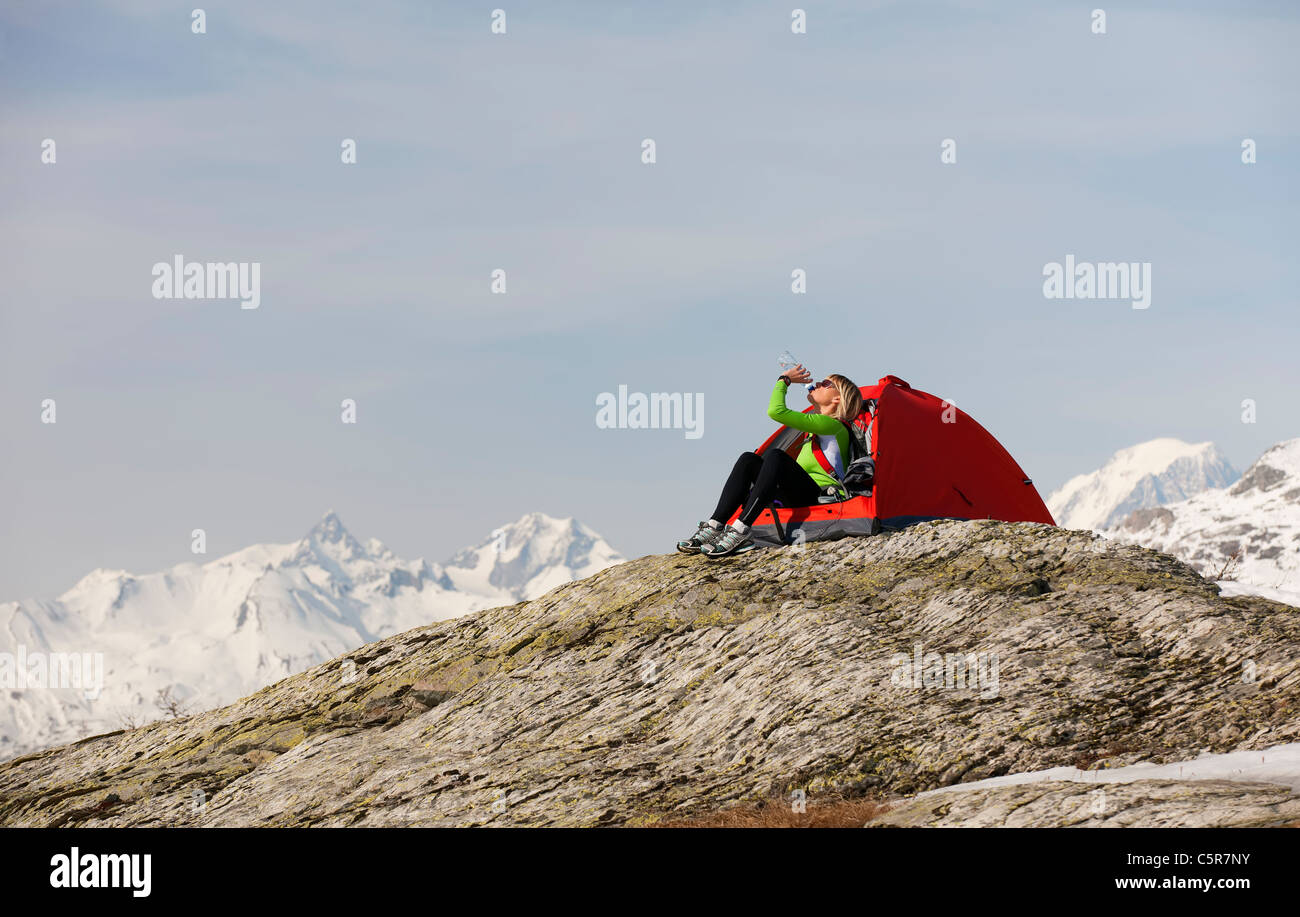 Eine Frau, die im verschneiten Hochgebirge Flüssigkeit trinken camping Re-Hydrat. Stockfoto