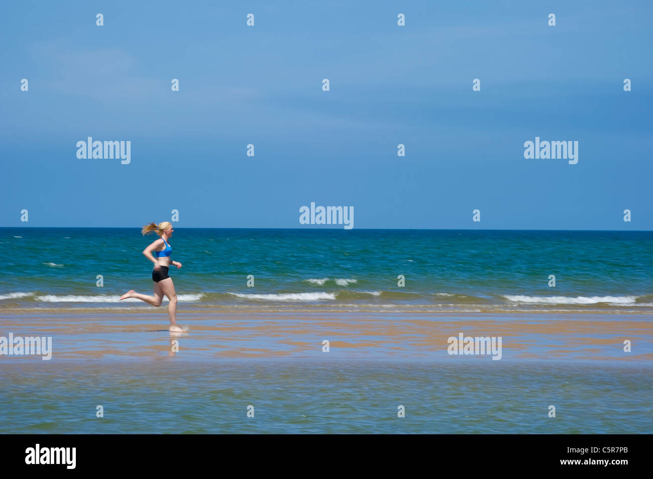 Ein Jogger, die entlang einer Sandes spucken in den Ozean. Stockfoto