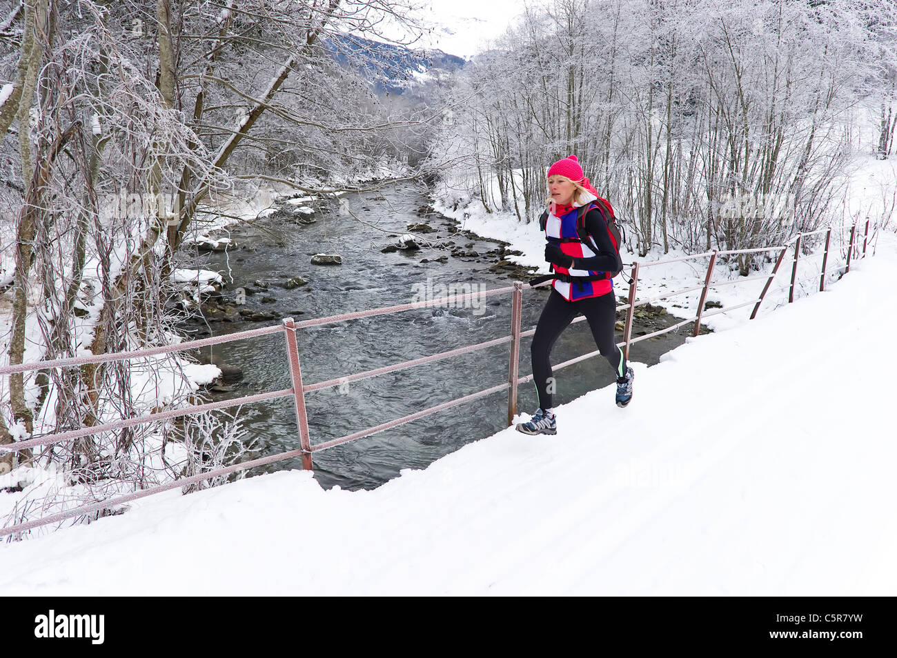 Eine Frau auf einer Brücke über einen schneereichen Winter Fluss joggen. Stockfoto
