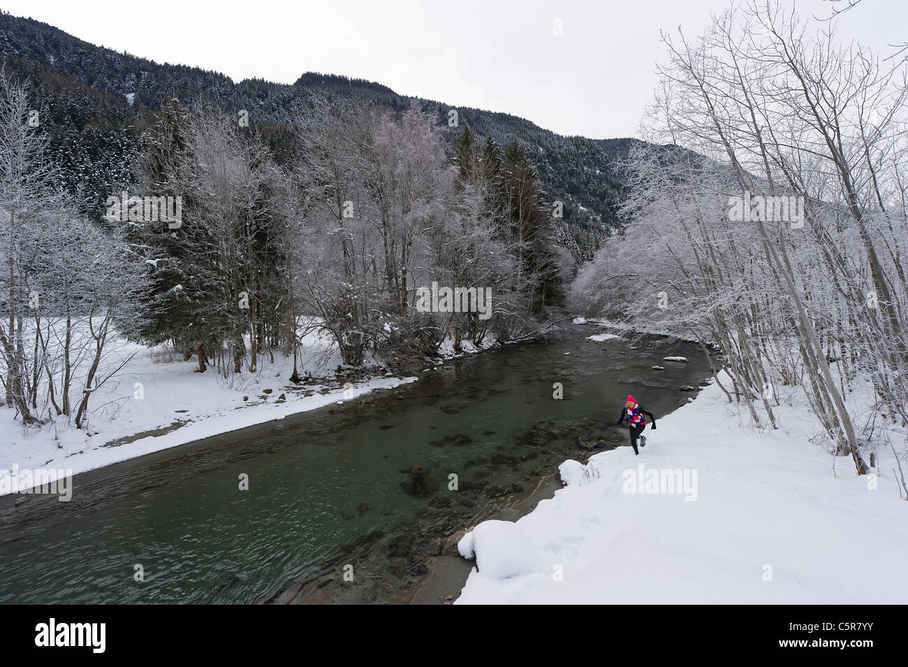 Ein Läufer an einem verschneiten Fluss entlang joggen. Stockfoto