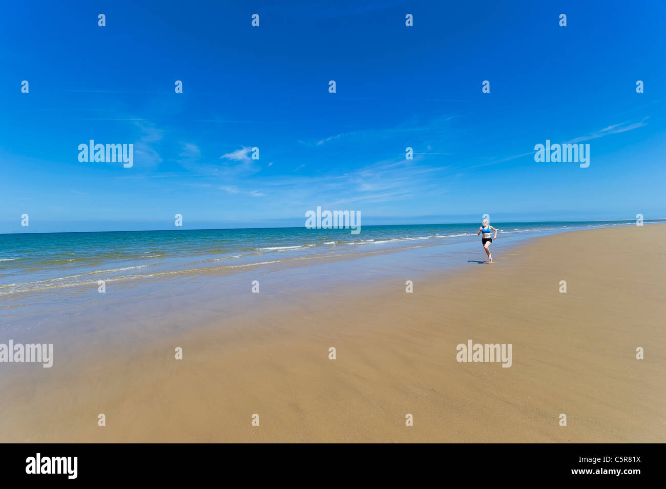 Eine Frau, die neben dem Meer an einem großen Sandstrand barfuß barfuß laufen Stockfoto