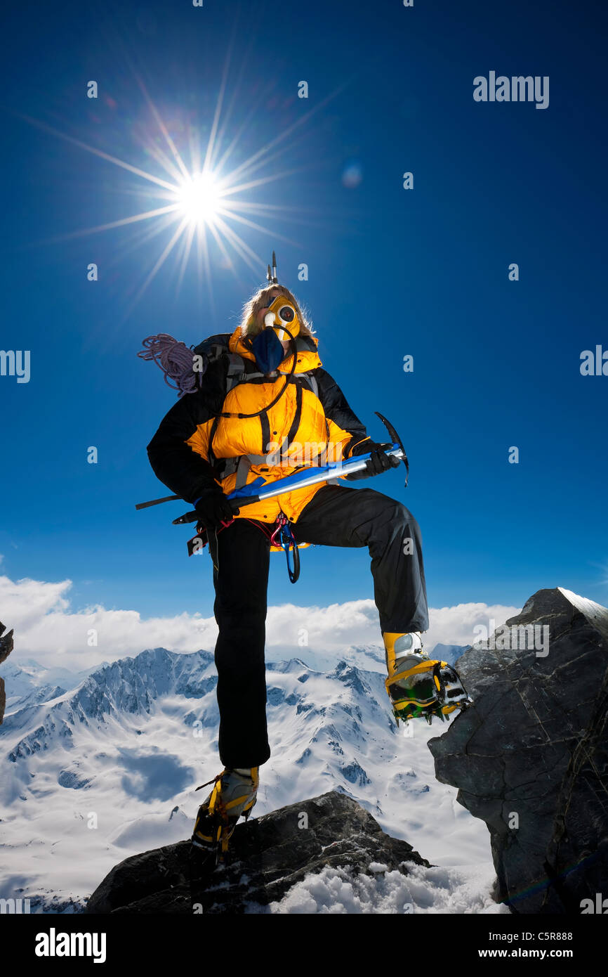 Ein Bergsteiger klettert über die Felsen auf sehr hohen schneebedeckten Berg über den Wolken. Stockfoto