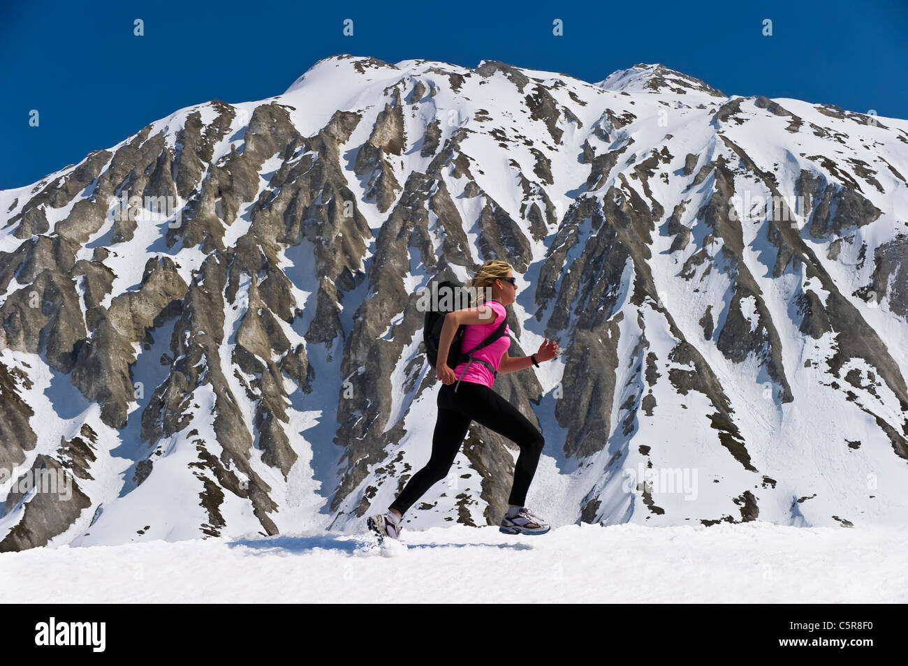 Jogger führt vorbei an einem beeindruckenden schneebedeckten Berge. Stockfoto