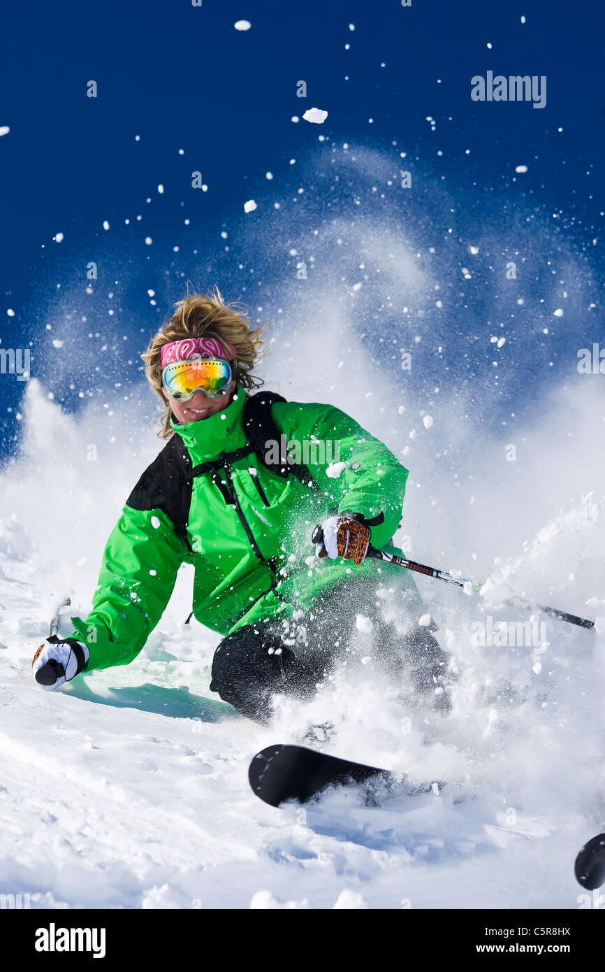 Eine Skifahrerin lächelt wie She Skis schwer durch die explodierenden Pulverschnee. Stockfoto