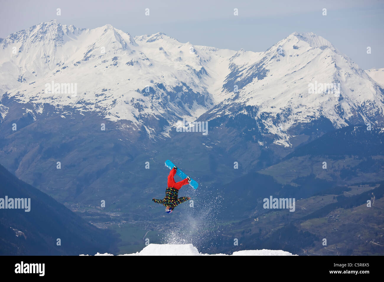 Ein Snowboarder wirft eine Umarmung Back Flip von einem verschneiten Berg. Stockfoto