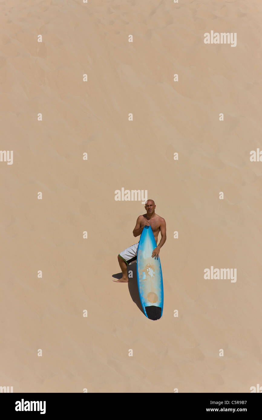 Surfer steht auf Düne mit Surfbrett. Stockfoto