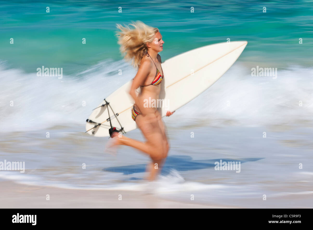 Eine junge blonde Surfer entlang der Meeresbrandung mit Surfbrett. Stockfoto