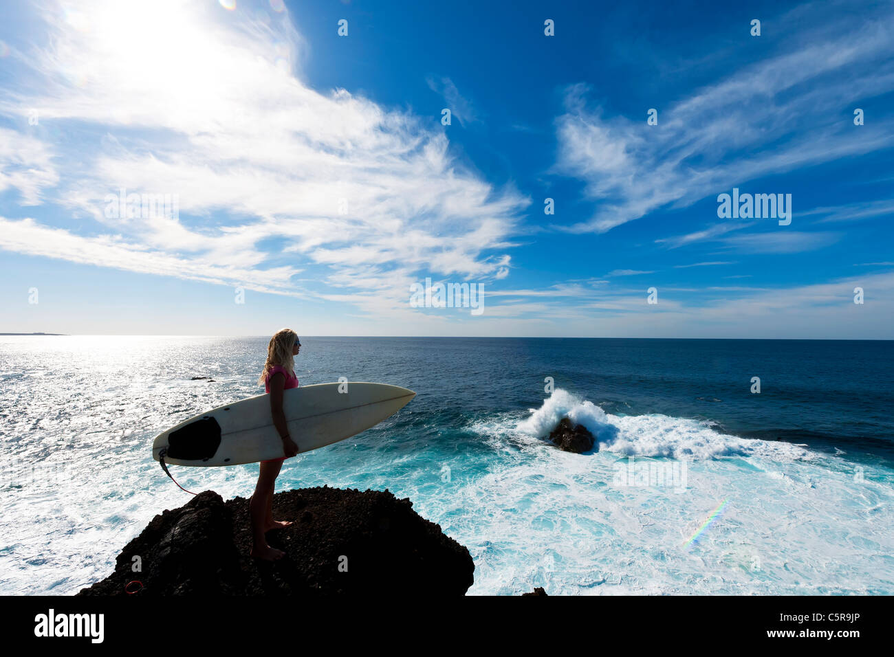 Ein Surfer steht und blickt auf das Meer an den brechenden Wellen. Stockfoto