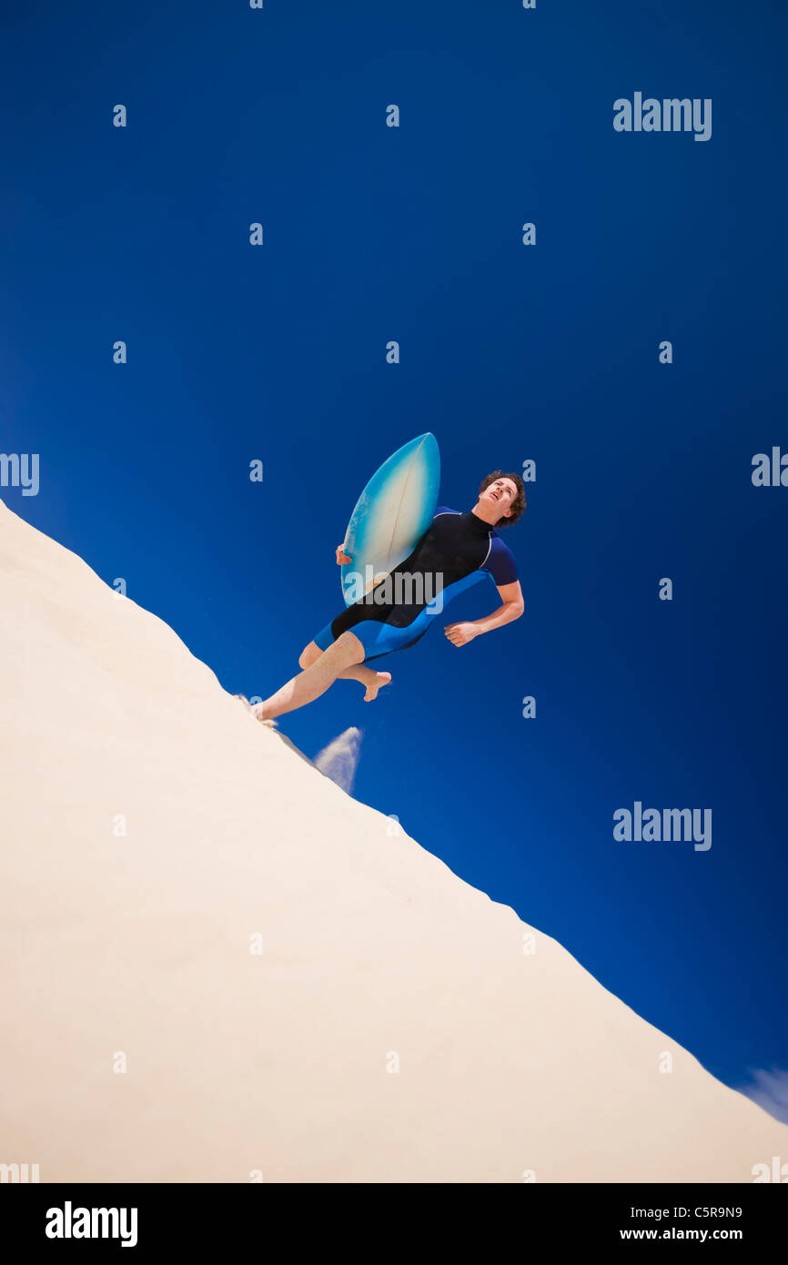 Junger Mann läuft über Surf-Dünen zum Meer mit Surfbrett. Stockfoto