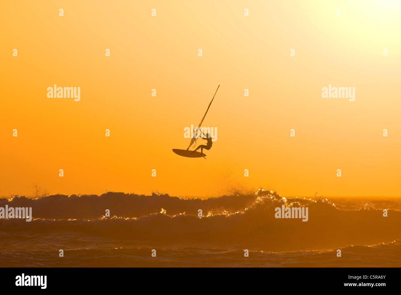 Ein Windsurfer springt eine Ozeanwelle in einem Sonnenuntergang. Stockfoto