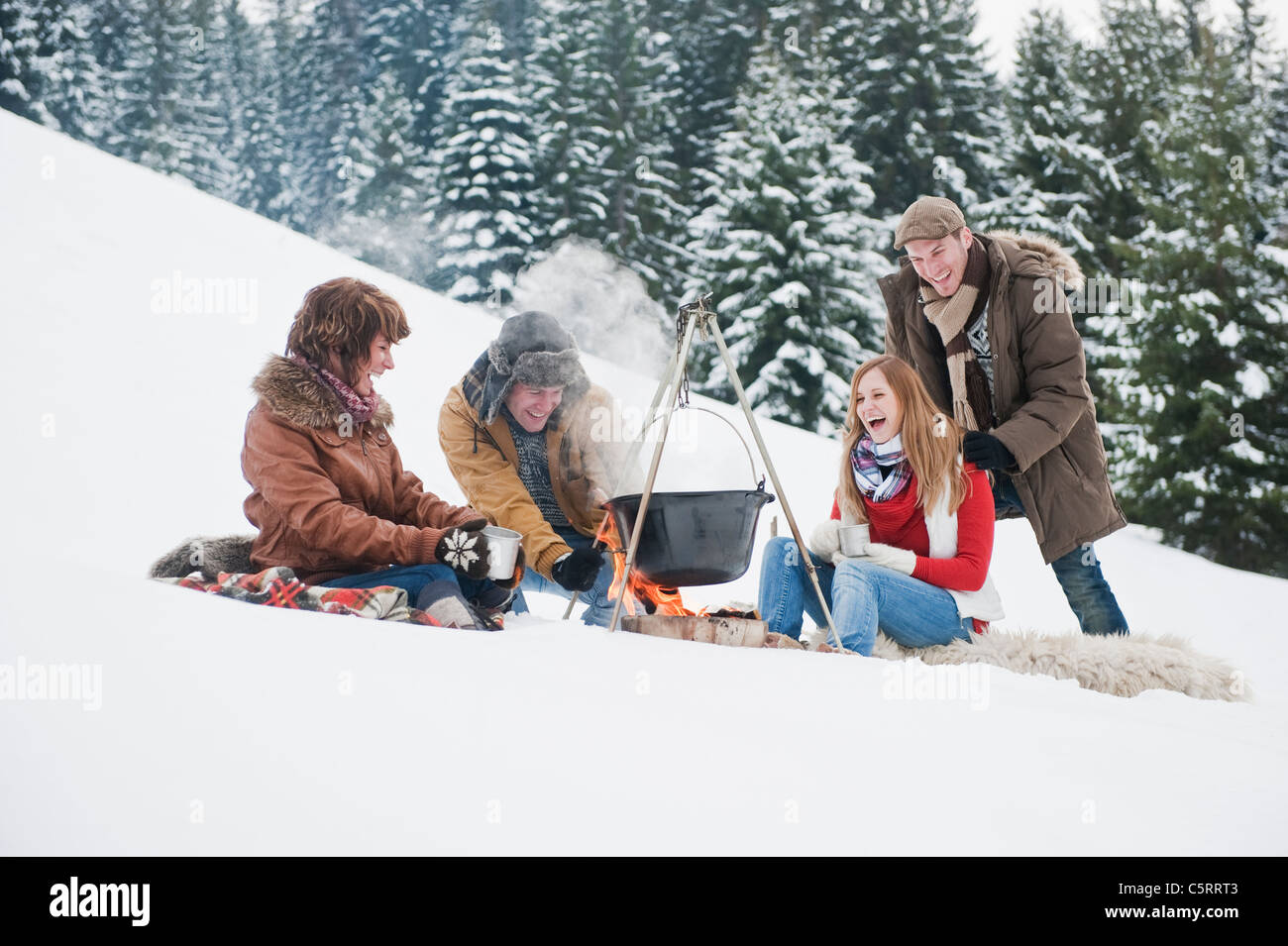 Österreich, Salzburger Land, Flachau, junge Männer und Frauen sitzen in der Nähe von Kamin und Zubereitung von Tee im Schnee Stockfoto