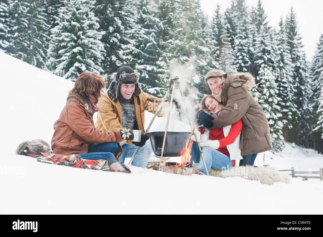 Österreich, Salzburger Land, Flachau, junge Männer und Frauen sitzen in der Nähe von Kamin und Zubereitung von Tee im Schnee Stockfoto