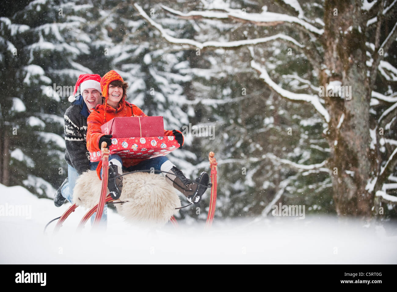 Österreich, Salzburger Land, Flachau, junge Frau sitzt auf Schlitten mit Weihnachten Pakete und Mann schieben Stockfoto