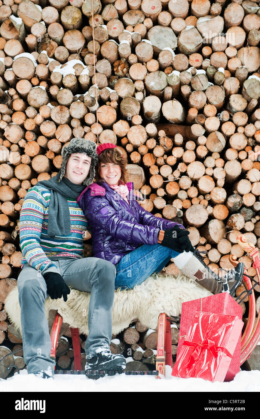 Österreich, Salzburger Land, Flachau, junger Mann und Frau sitzen auf Schlitten mit Weihnachtsgeschenk und Brennhölzer im Hintergrund Stockfoto