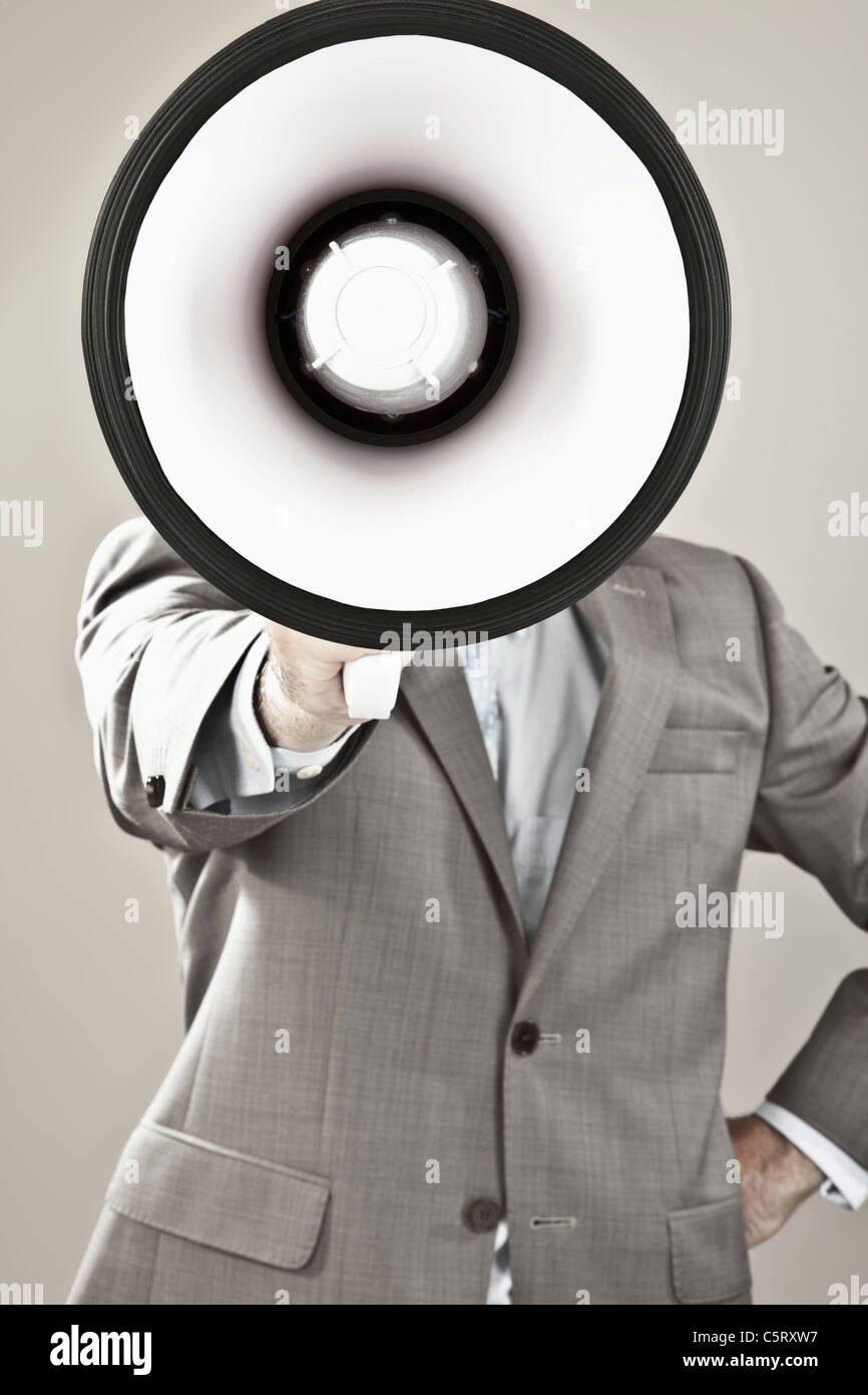 Nahaufnahme von Geschäftsmann mit Gesicht bedeckt mit Megaphon vor grauem Hintergrund Stockfoto