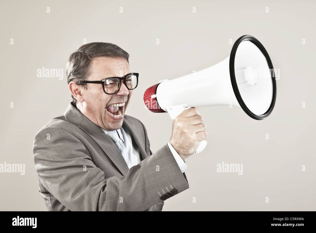 Nahaufnahme von Geschäftsmann schreien über Megaphon vor grauem Hintergrund Stockfoto