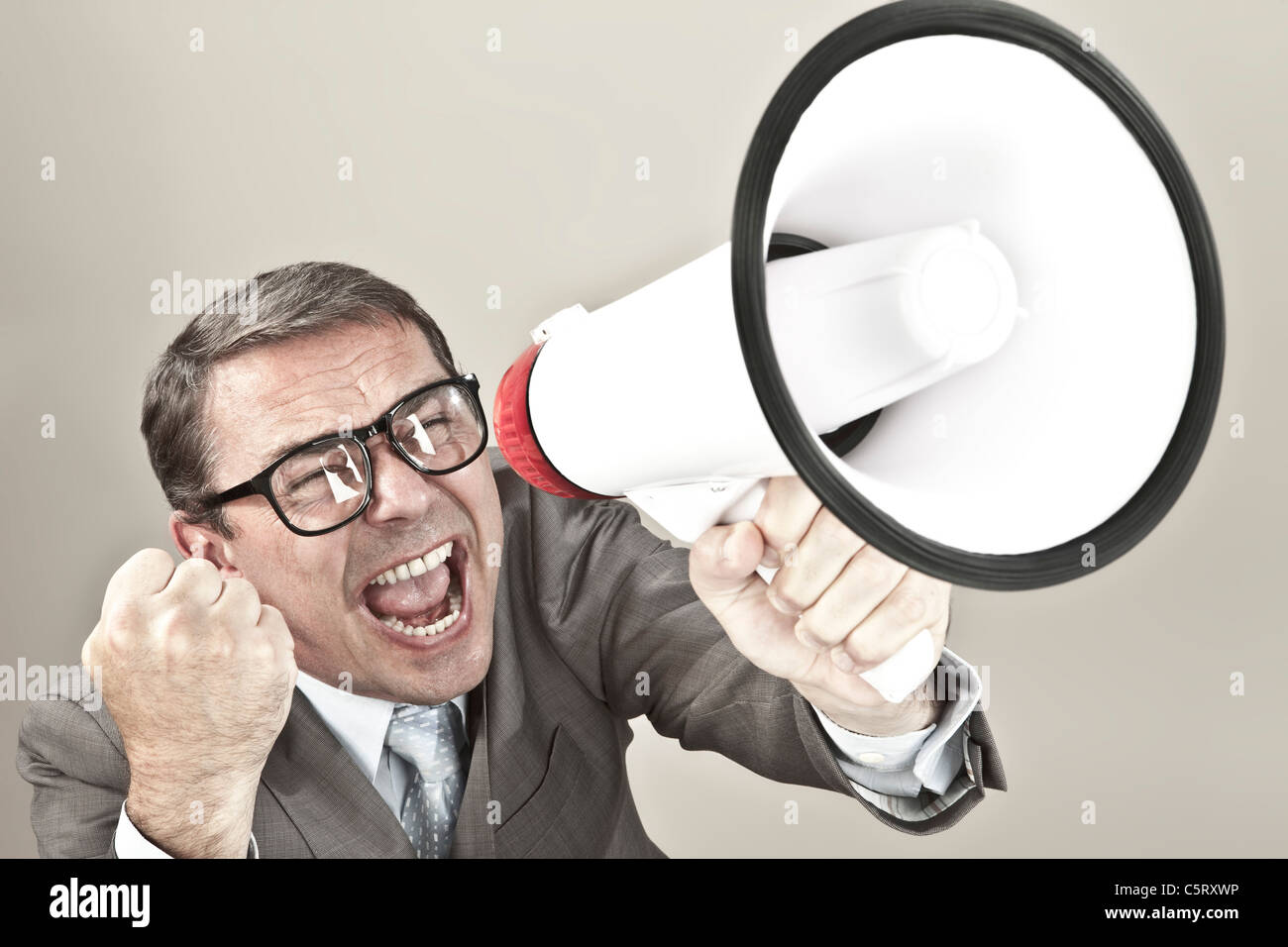 Nahaufnahme von Geschäftsmann schreien über Megaphon vor grauem Hintergrund Stockfoto