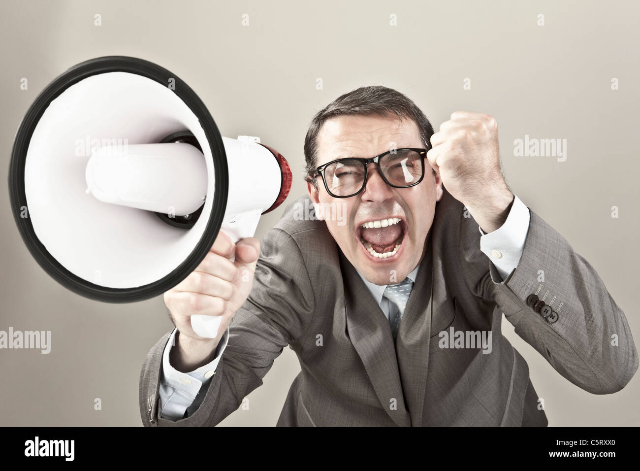 Nahaufnahme von Geschäftsmann schreien über Megaphon vor grauem Hintergrund Stockfoto