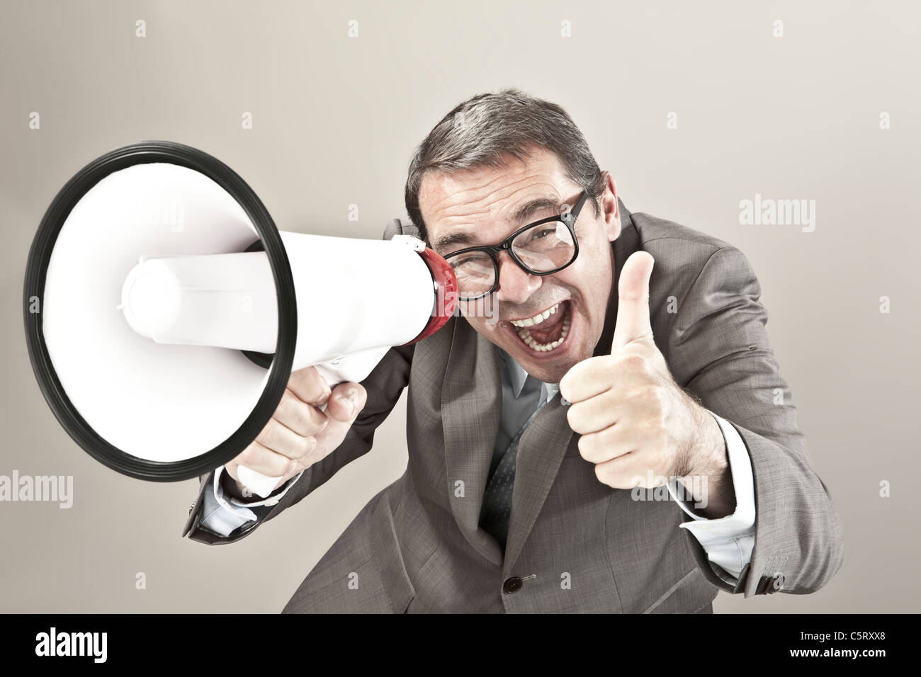 Nahaufnahme von Geschäftsmann schreien über Megaphon vor grauem Hintergrund Stockfoto