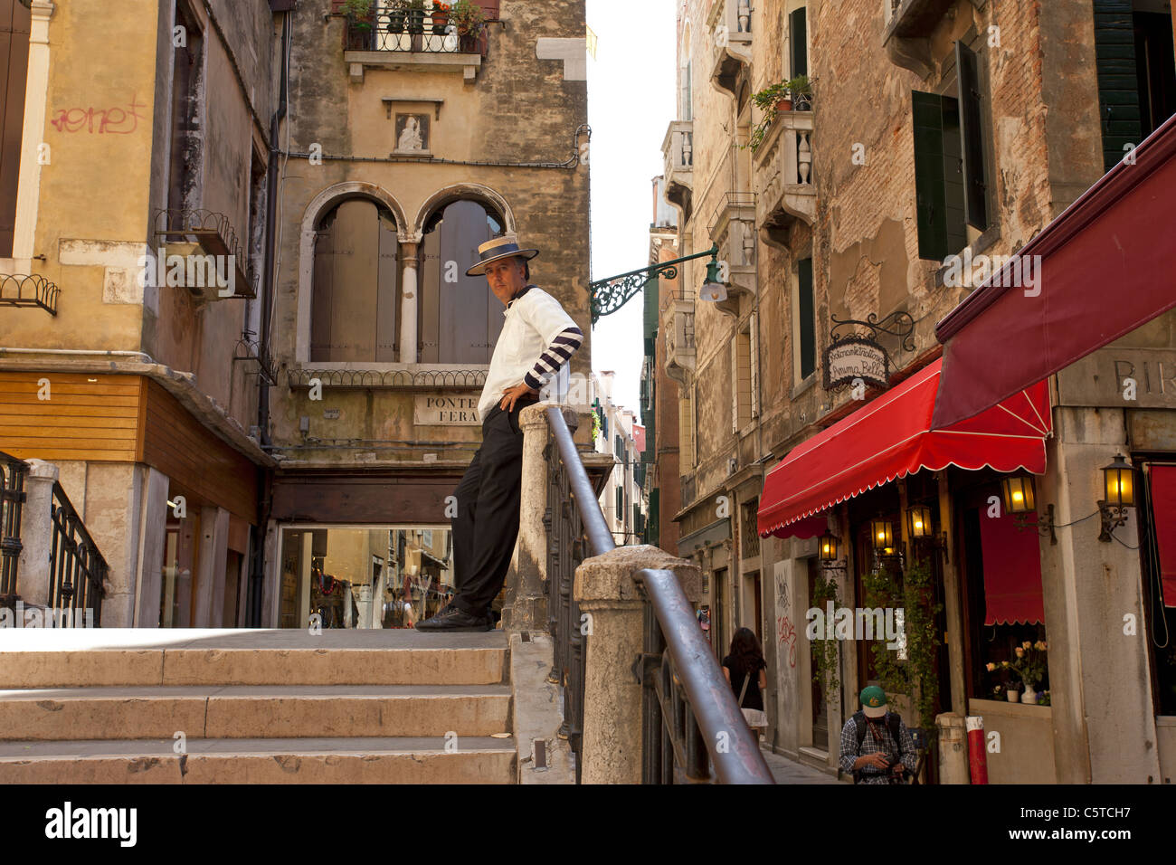 Gondoliere gekleidet in einheitlichen warten auf eine kleine Brücke in Venedig, Italien für Kunden zu kommen.  Restaurants und Geschäfte. Stockfoto