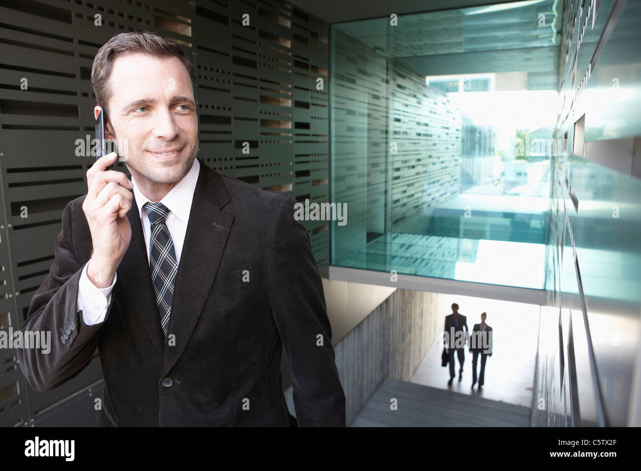 Deutschland, Köln, Geschäftsmann im Treppenhaus mit Handy, Business-Leute im Hintergrund Stockfoto
