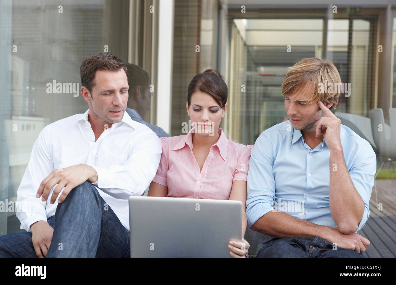 Deutschland, Köln, drei Geschäftsleute sitzen nebeneinander, mit laptop Stockfoto