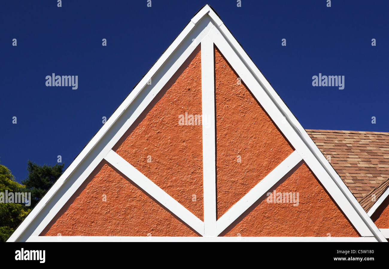 Weißes Holz Dreieck Design ein Tudor Haus gegen eine rote Wand mit blauem Himmel Stockfoto
