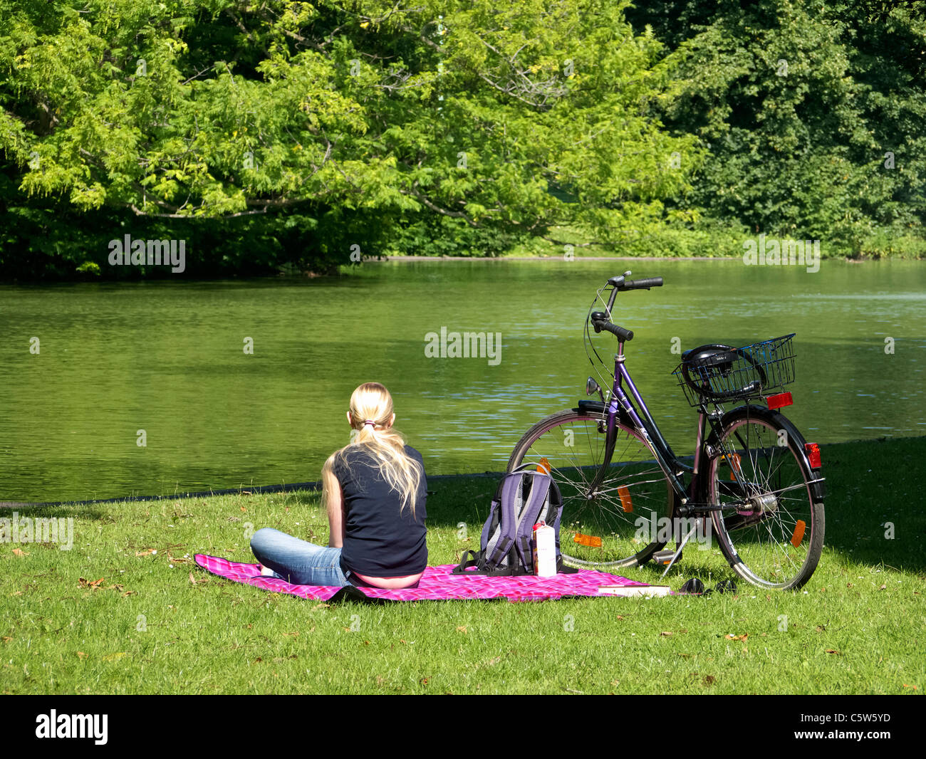 Junge Frau sitzt neben See im Volksgarten-Park in Köln Stockfoto