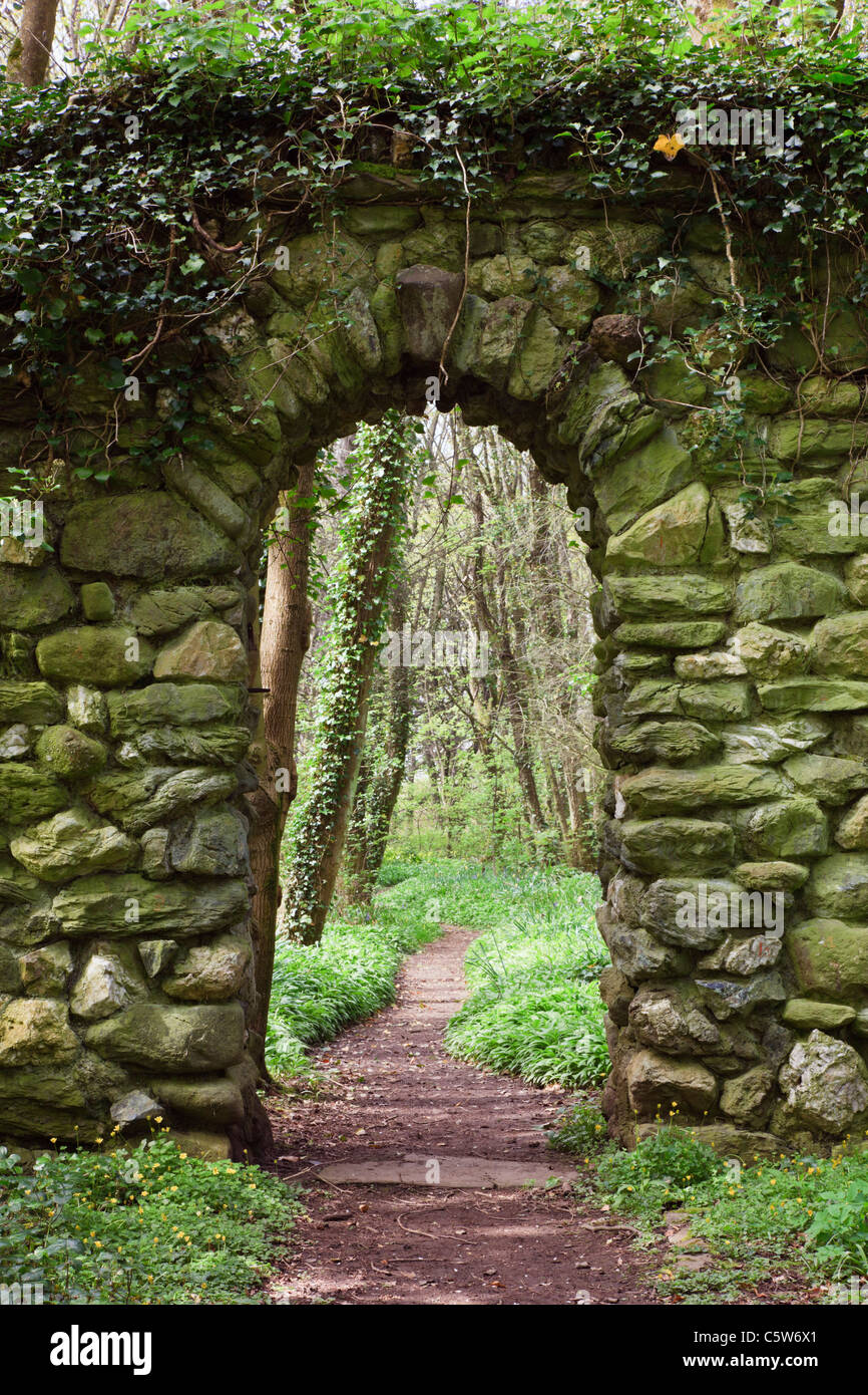 Blick durch eine Mauer aus Stein Bogen über einen leeren Garten Weg in den Wald führt. Anglesey Wales England Großbritannien Stockfoto