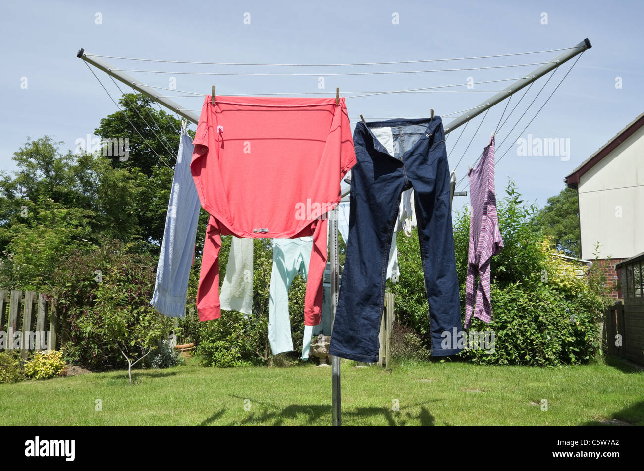 Nasse Haushaltskleidung, die an einer Drehwaschleitung hängend ist, um an einem warmen sonnigen Tag im Freien in einem heimischen Garten zu trocknen. Großbritannien. Stockfoto