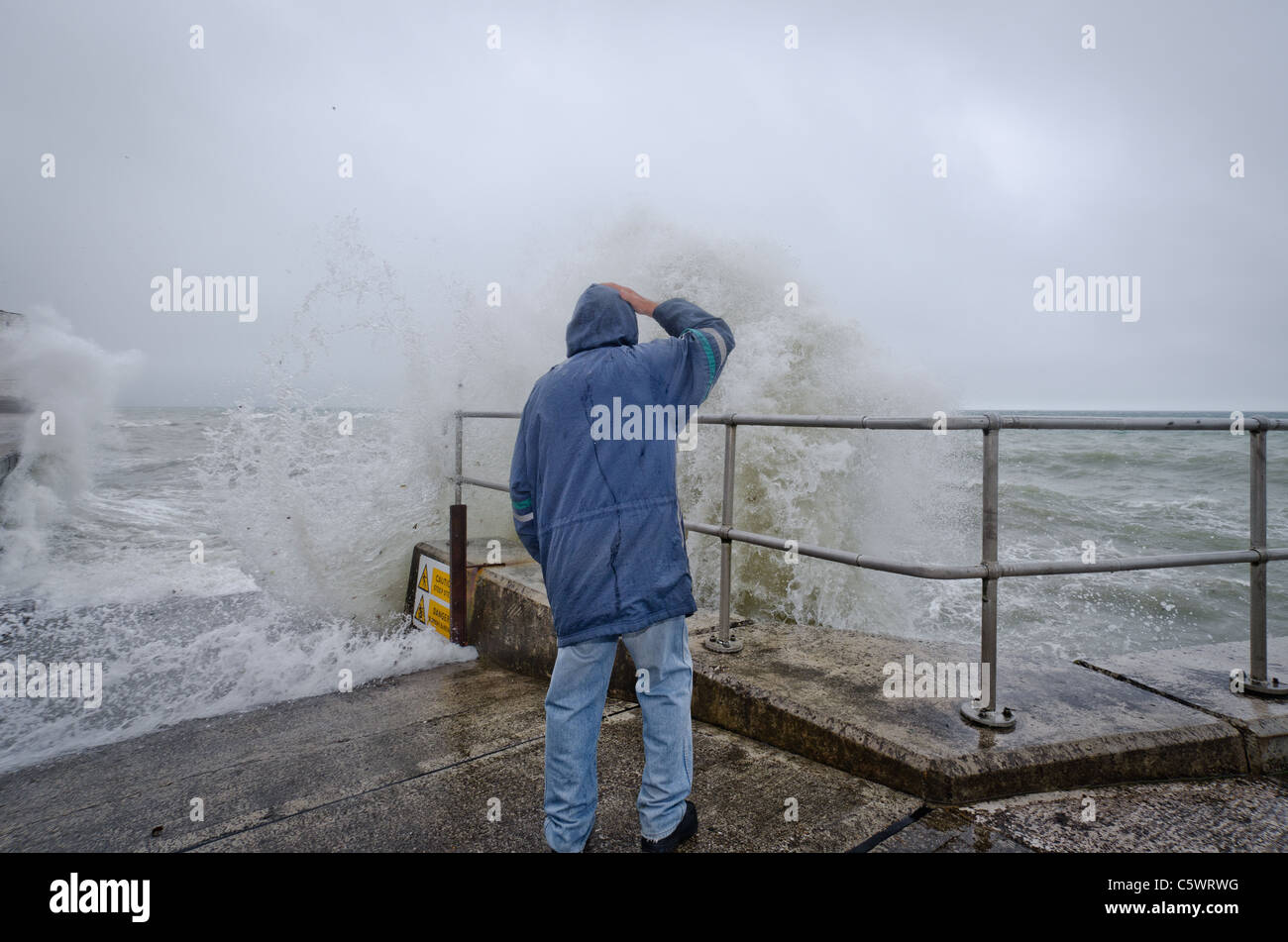 Ein Mann trotzt das stürmische Wetter Saltdean, Ast East Sussex, Promenade, wie Wellen auf die Mole treffen. Stockfoto