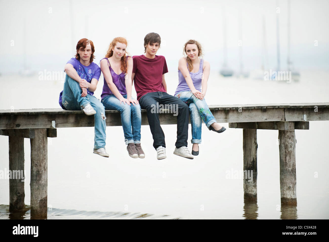 Deutschland, Bayern, Ammersee, vier Freunde sitzen auf Steg Stockfoto