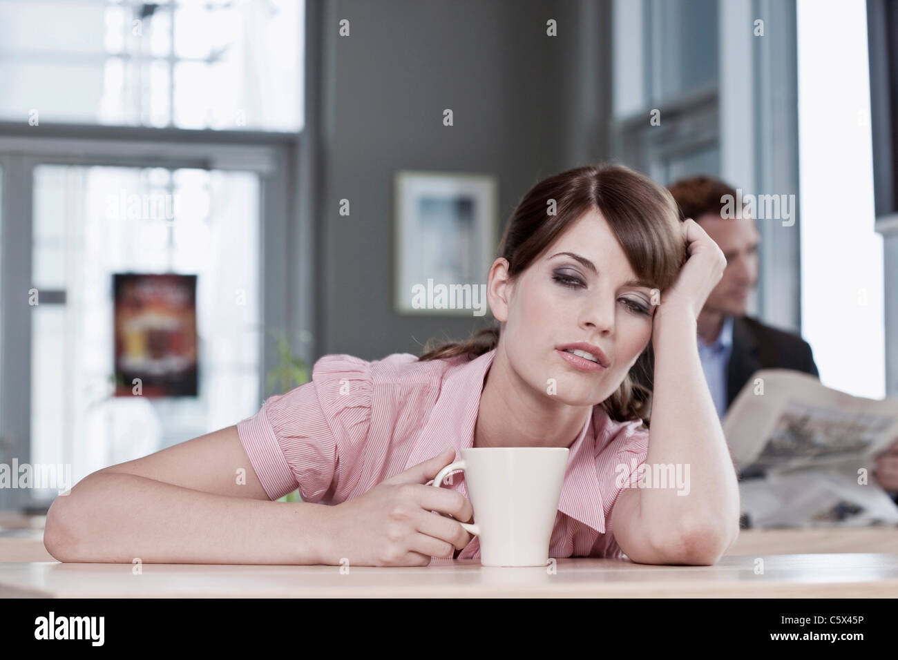 Deutschland, Köln, Frau sitzen im Café, Mann im Hintergrund lesen Zeitung Stockfoto