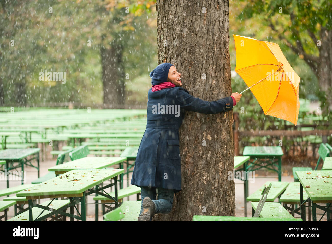 Deutschland, Bayern, München, englischer Garten, Frau im Biergarten Baum umarmen, halten Regenschirm, lachen Stockfoto