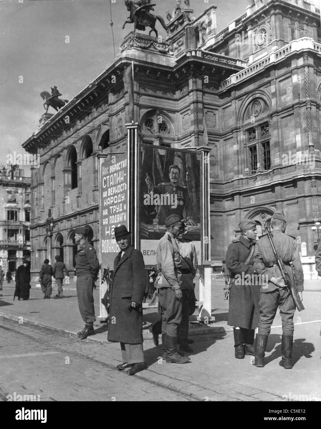 Wien 1945 überblickt Outside the Opera House ein Bild von Stalin während ein US-Soldaten auf der linken Seite steht eine Gruppe von sowjetischen Soldaten Stockfoto